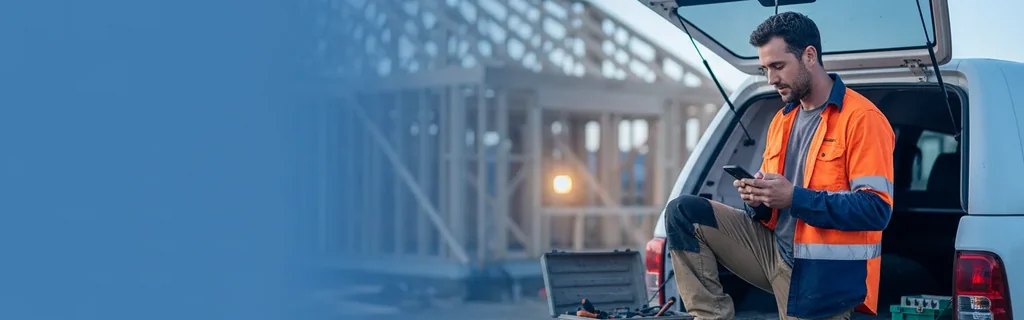 Contractor sitting on a ute tailgate at a residential build site, checking his phone